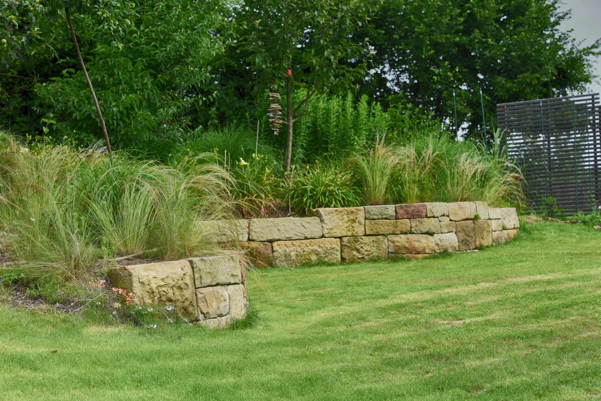 Rasenfläche mit Natursteinmauer und Ziergräsern